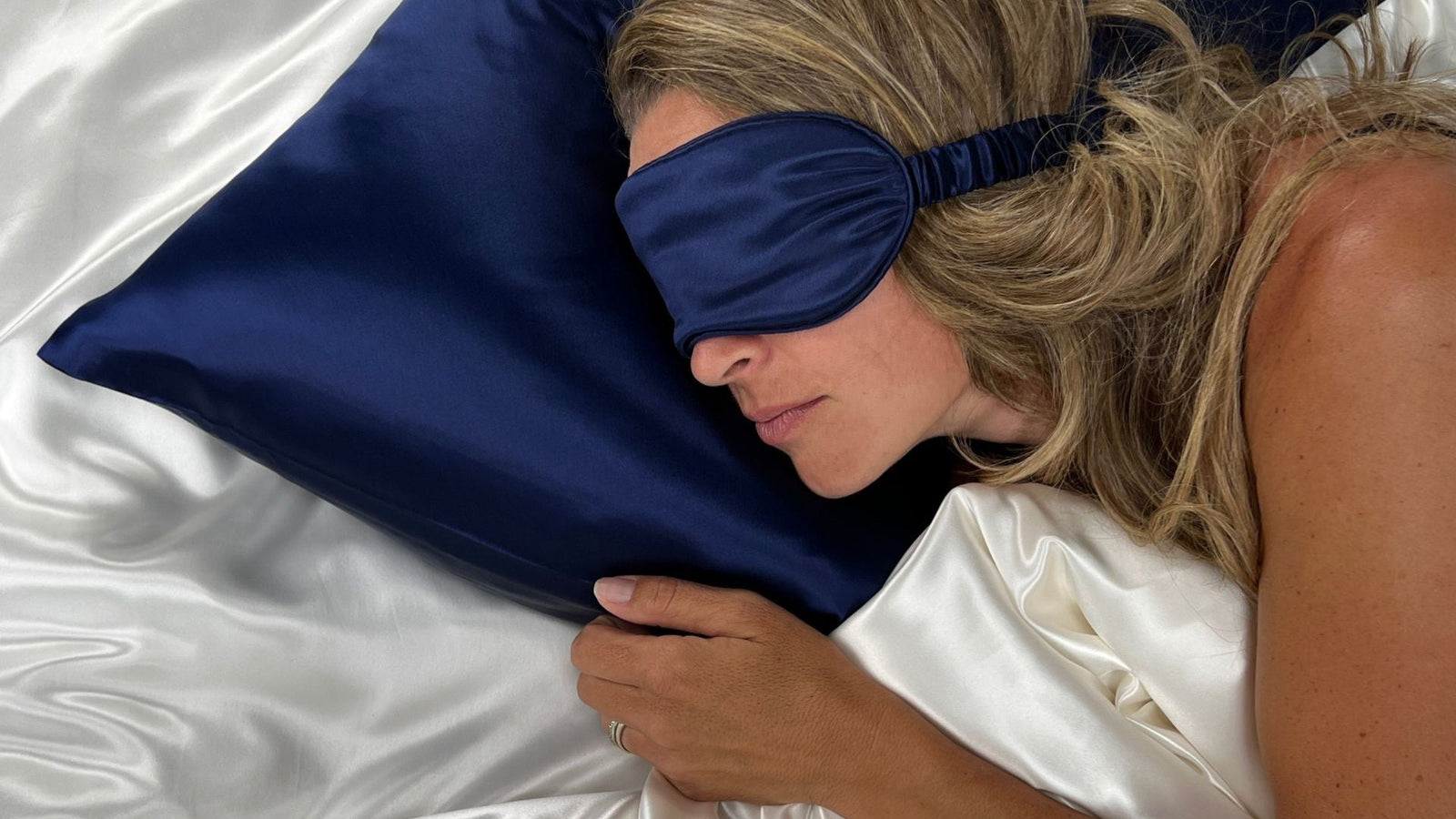 Model in navy silk sleep mask sleeping on matching navy pillowcase