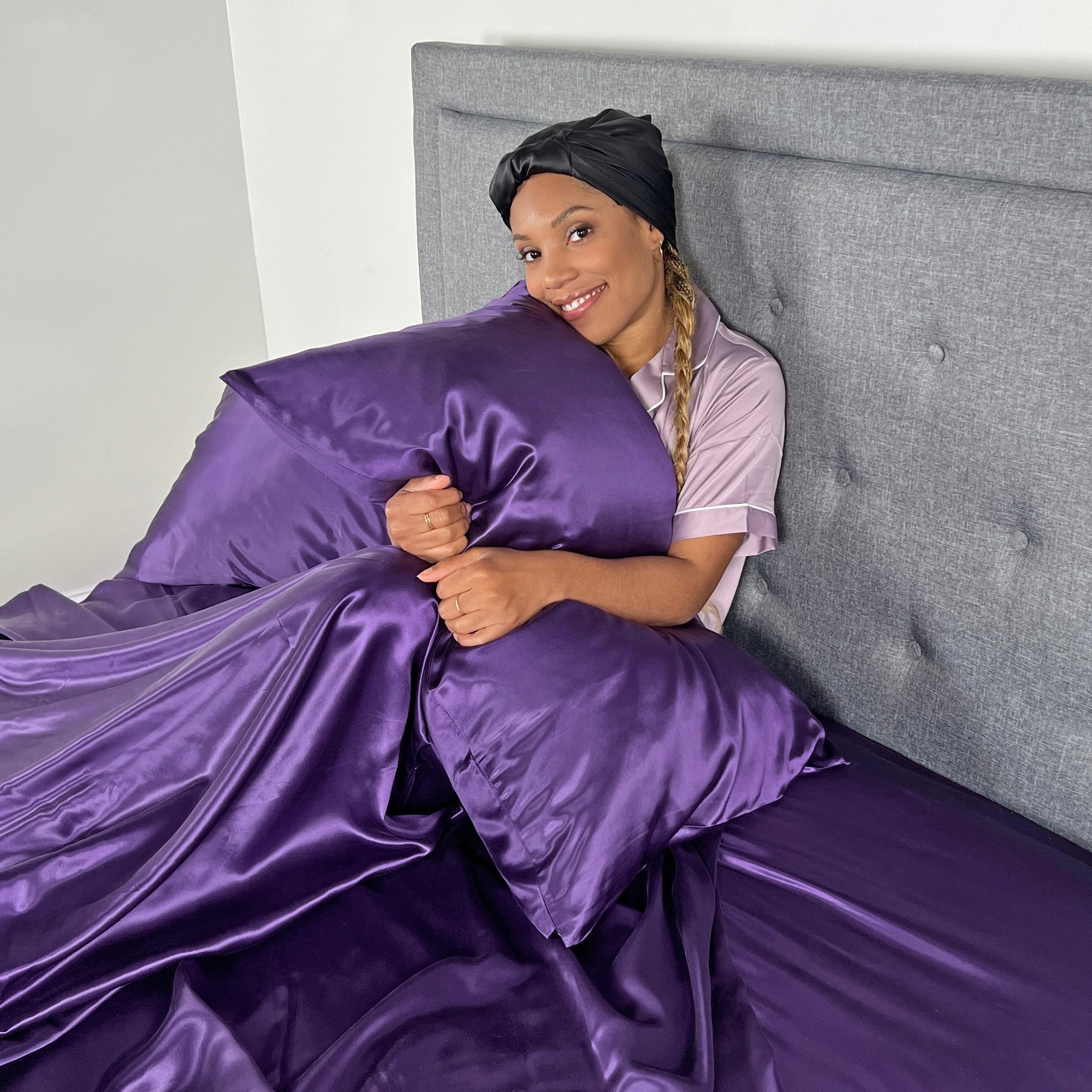Woman smiling while hugging a pillow on the twin bed sheets with a soft, luxurious silk sheet set