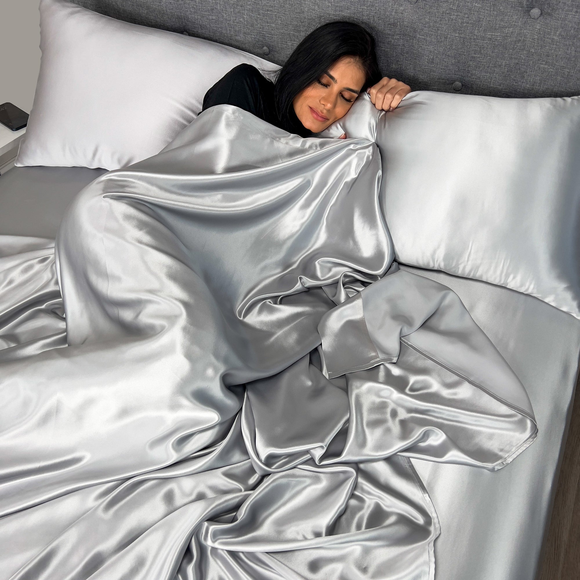 Silver silk flat sheet draped over a neatly made bed in a bright, modern bedroom