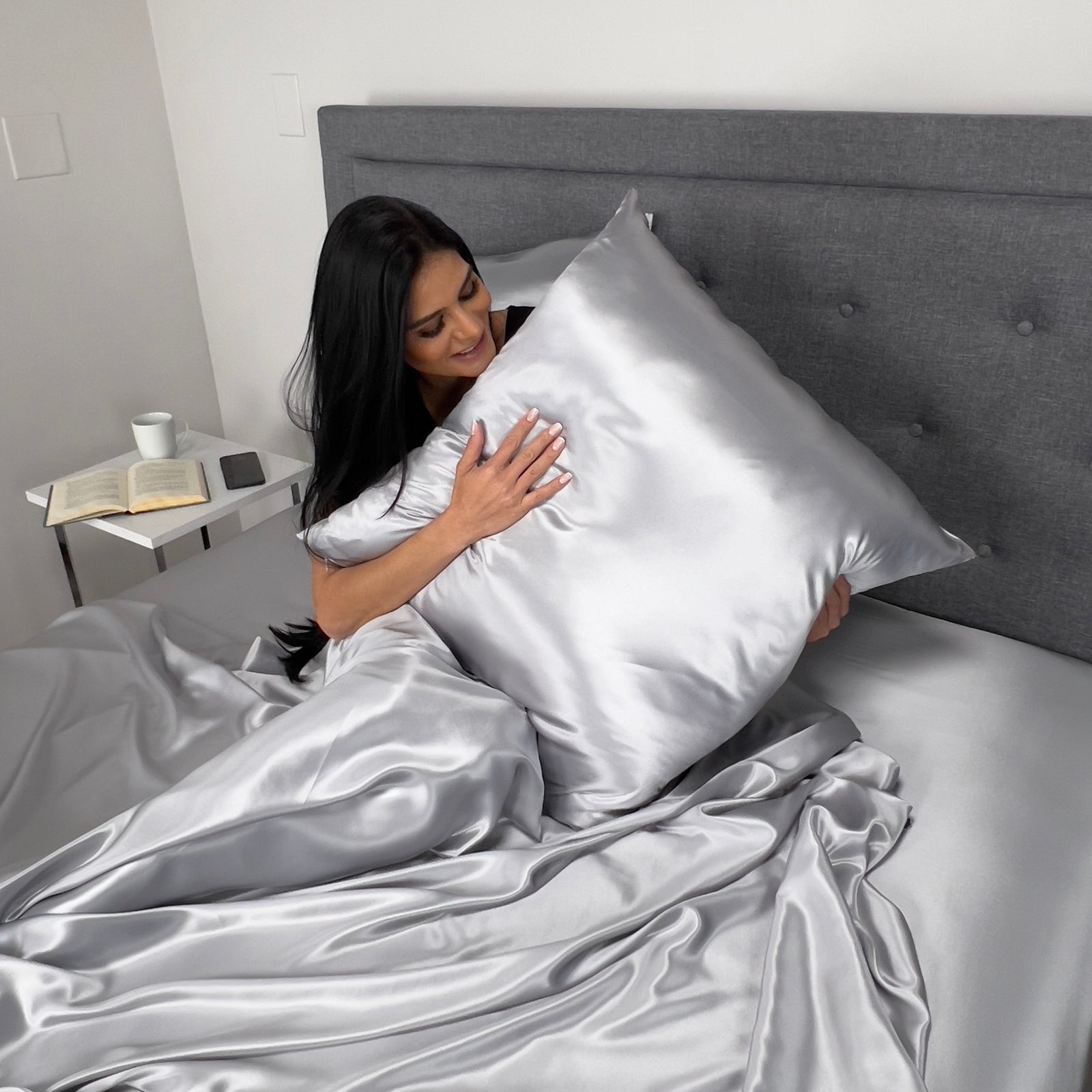 Woman sitting on bed holding with Silver Euro sham, enjoying luxurious comfort